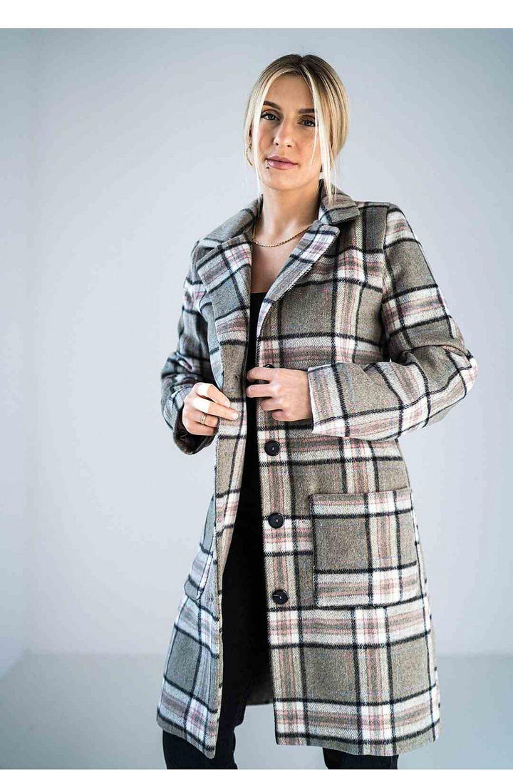 A beige plaid longline coat with a classic button-up design, large front pockets, and a tailored fit, worn by a woman with blonde hair styled in a low bun.






