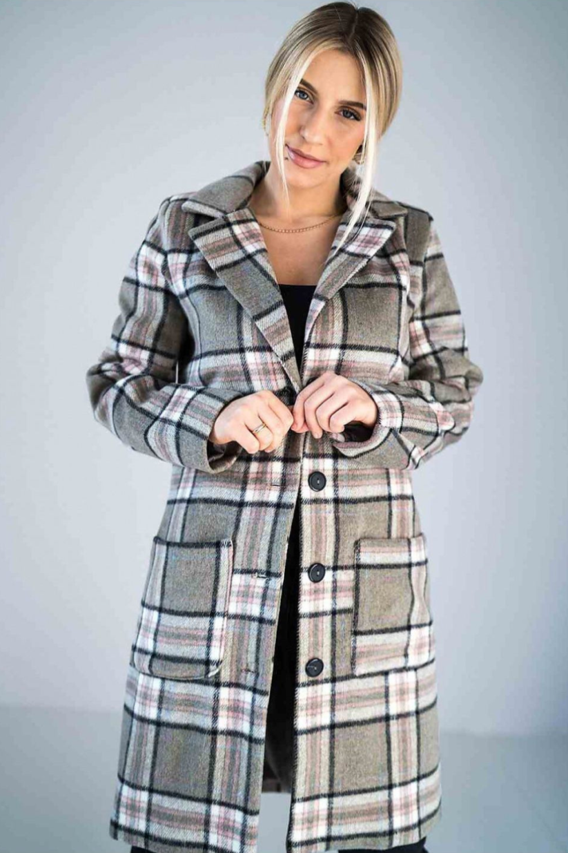 A beige plaid longline coat with a classic button-up design, large front pockets, and a tailored fit, worn by a woman with blonde hair styled in a low bun.






