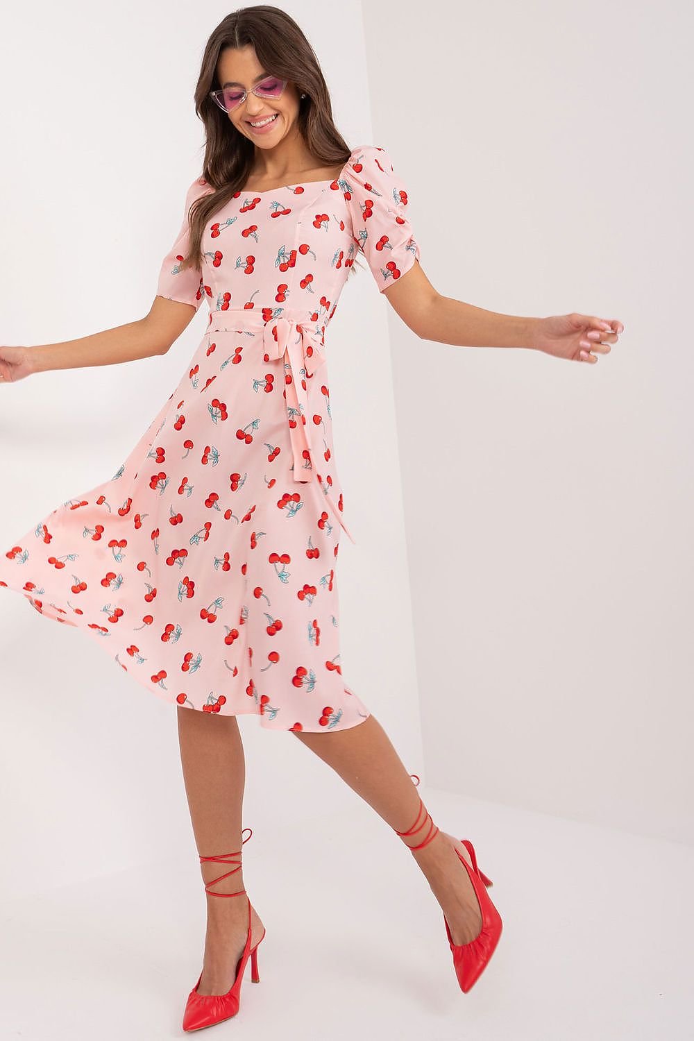 Flared summer youth dress featuring a playful cherry print, heart-shaped neckline, buff sleeves, tie belt, and discreet back zipper