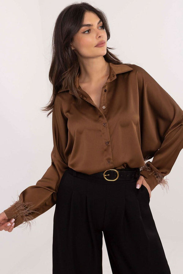 An elegant women's shirt with a classic cut, designed for special occasions and office stylings. Made of a blend of polyester and viscose, it provides comfort and a perfect look throughout the day. The smooth fabric emphasizes its subtle style, while the long length adds elegance and slims the silhouette. The long sleeves with cuffs adorned with decorative feathers give the shirt a unique, refined character, perfect for business meetings or evening outings. The shirt has a classic collar and side slits