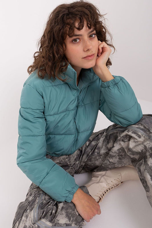 A short quilted jacket with a zip closure, long sleeves, and side slip pockets. Fully lined for added comfort, it features a non-removable hood discreetly tucked into the collar, combining practicality with style.