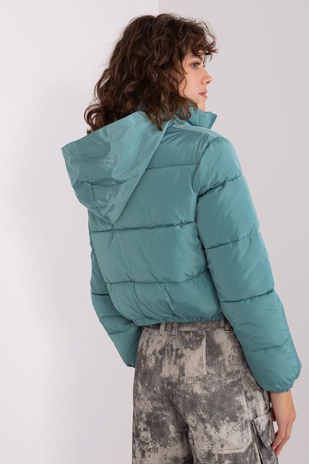 A short quilted jacket with a zip closure, long sleeves, and side slip pockets. Fully lined for added comfort, it features a non-removable hood discreetly tucked into the collar, combining practicality with style.