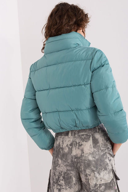 A short quilted jacket with a zip closure, long sleeves, and side slip pockets. Fully lined for added comfort, it features a non-removable hood discreetly tucked into the collar, combining practicality with style.