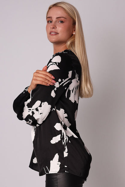 Elegant long sleeve blouse with a ruffled black and white print, low collar, button closure, and elastic cuffs, ideal for casual and semi-casual occasions.
