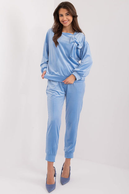 A stylish velour set featuring a sweatshirt with a decorative bow and round neckline, paired with high-waisted pants with a waist tie, side pockets, and leg welts, offering comfort, elegance, and versatility for casual outfits.