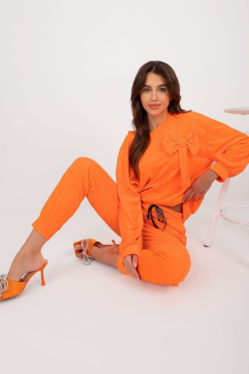 A stylish velour set featuring a sweatshirt with a decorative bow and round neckline, paired with high-waisted pants with a waist tie, side pockets, and leg welts, offering comfort, elegance, and versatility for casual outfits.