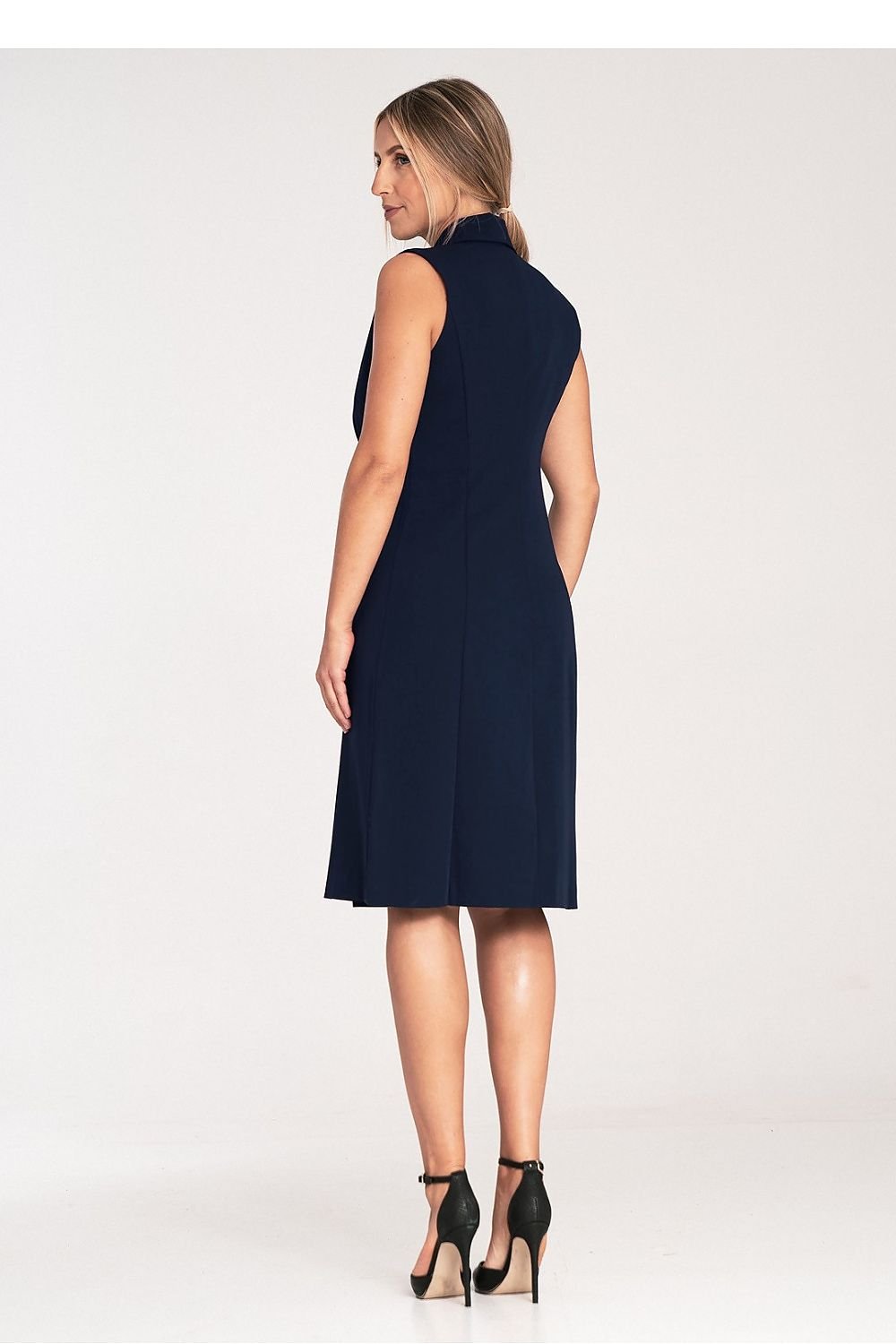 An elegant sleeveless midi dress with narrow lapels, an envelope neckline, a double-breasted closure featuring large decorative snaps, and a slightly flared hem.






