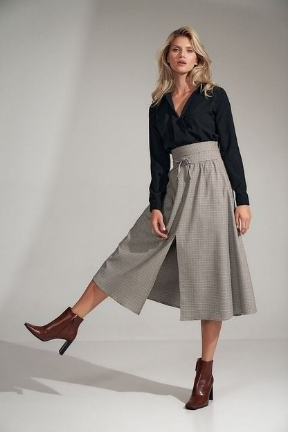 A long, flared pleated plaid skirt with a wide high waist, decorative binding, and a front slit. Fastened with a covered zip at the left side.

