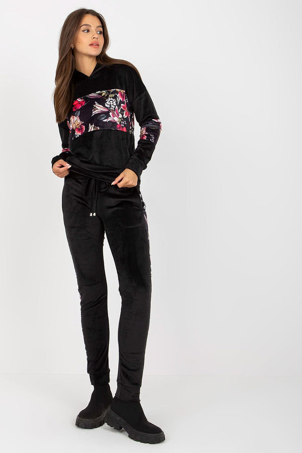 A stylish velour set featuring a hooded sweatshirt with long sleeves, paired with long pants with a waist tie and slip pockets, adorned with decorative floral inserts for a feminine touch.






