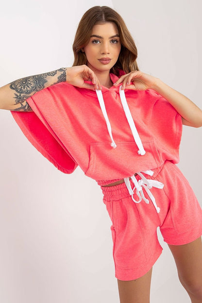 Comfortable pink tracksuit set featuring a hooded blouse with short wide sleeves and a kangaroo pocket, paired with shorts that have a waist tie and slip pockets. Ideal for casual wear.