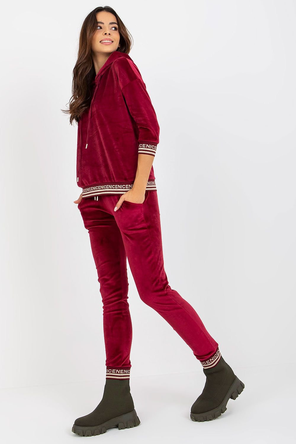 A stylish women's velour set featuring a hoodie with 3/4 sleeves, paired with long pants that have a waist tie and slip pockets. The set is finished with ribbed cuffs, adorned with a decorative print for added flair.


