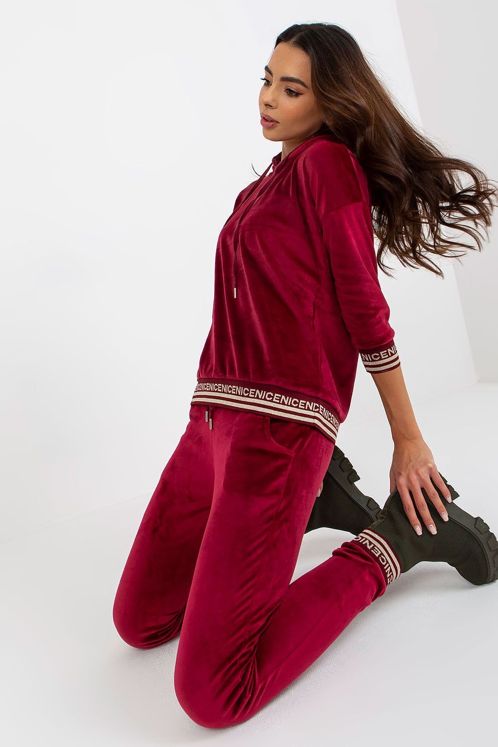 A stylish women's velour set featuring a hoodie with 3/4 sleeves, paired with long pants that have a waist tie and slip pockets. The set is finished with ribbed cuffs, adorned with a decorative print for added flair.


