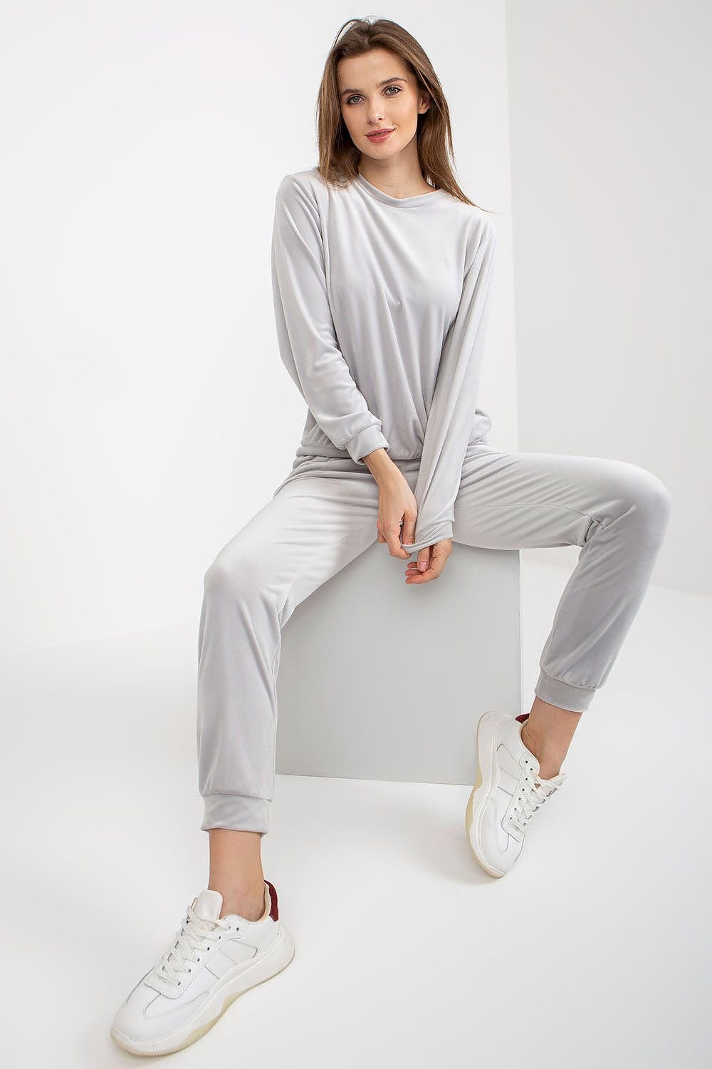 A ladies' velour set featuring a long-sleeve blouse that is tucked in over the head, paired with long pants with an elastic waistband and slip pockets on the sides for added convenience.






